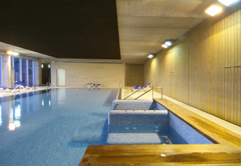 Piscina cubierta en alojamiento glamping, con jacuzzi, tumbonas y paredes de madera bajo iluminación.