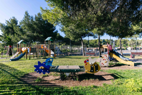 Parque infantil con toboganes, columpios y juegos bajo árboles en un alojamiento de glamping durante el día.