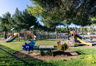 Parque infantil con toboganes, columpios y juegos bajo árboles en un alojamiento de glamping durante el día.