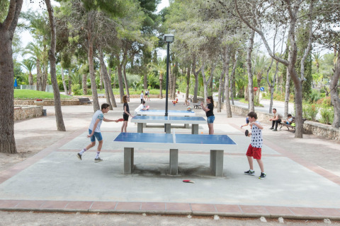 Niños y adultos juegan tenis de mesa al aire libre bajo los árboles en un área recreativa de glamping.