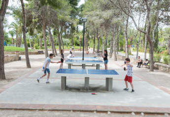 Niños y adultos juegan tenis de mesa al aire libre bajo los árboles en un área recreativa de glamping.