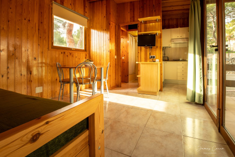 Interior luminoso de madera en Vilanova Park BUNGALOW 4 PAX S150 con cocina, mesa y ventanas grandes.
