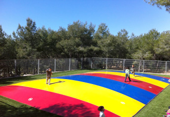 Kinderen spelen op een luchtkussen met felle kleuren bij een glampingverblijf in een groene omgeving.