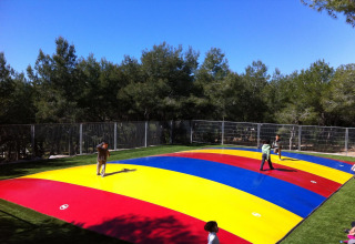 Niños juegan sobre un gran cojín de salto colorido en el exterior de un alojamiento glamping rodeado de árboles.