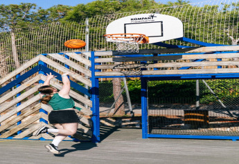 Una joven lanza una pelota de baloncesto a la canasta en una cancha al aire libre junto a un glamping.