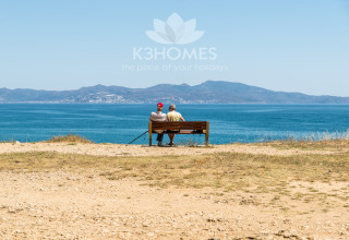 Two people sitting on a bench by the sea, enjoying mountain views at a scenic glamping accommodation.