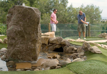 Twee mannen spelen minigolf bij een kunstmatig beekje en rotsen op een prachtige glampinglocatie.