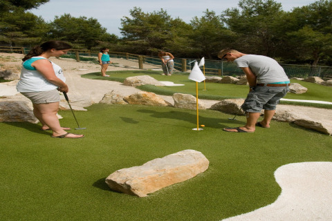 Cuatro personas juegan al minigolf en un campo exterior con rocas y árboles en un alojamiento glamping.