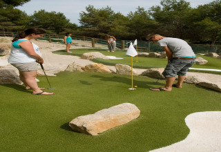 Cuatro personas juegan al minigolf en un campo exterior con rocas y árboles en un alojamiento glamping.