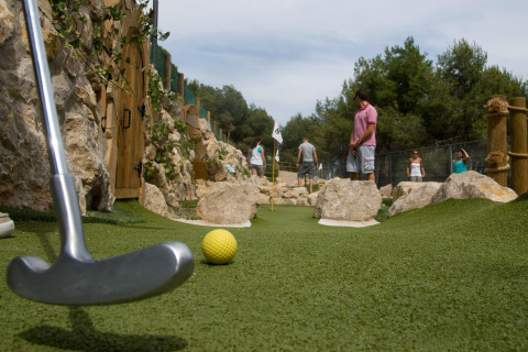 Personas juegan minigolf en una pista exterior rodeada de rocas en un alojamiento glamping.