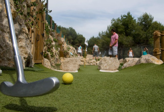 Personas juegan minigolf en una pista exterior rodeada de rocas en un alojamiento glamping.