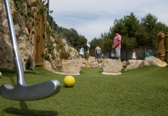 Personas juegan minigolf en una pista exterior rodeada de rocas en un alojamiento glamping.