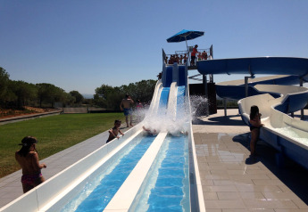 Kinderen en volwassenen amuseren zich op een waterglijbaan bij een glamping onder een stralende hemel.