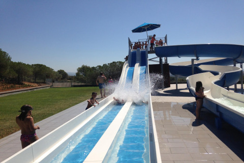 Niños y adultos se divierten en un tobogán de agua en un alojamiento glamping bajo un cielo despejado.