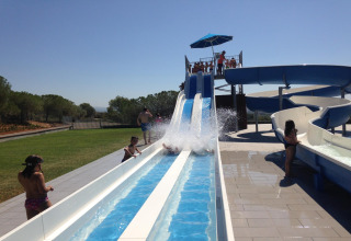 Niños y adultos se divierten en un tobogán de agua en un alojamiento glamping bajo un cielo despejado.