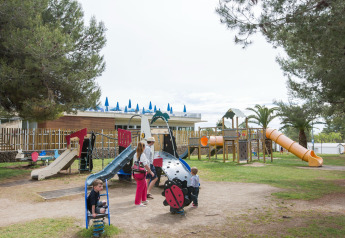 Spielplatz mit Kindern und Erwachsenen an einer Glamping-Unterkunft, umgeben von Bäumen und Natur.