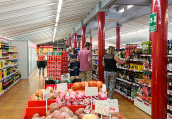 Mensen winkelen in een supermarkt bij een glampingverblijf, met verse producten en drank op de rekken.