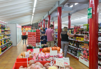 Personas comprando en un supermercado dentro de un alojamiento glamping, con vegetales y bebidas en estantes.