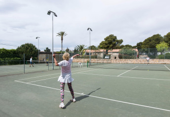 Frau spielt Tennis auf einem Außenplatz bei Glamping-Unterkunft, umgeben von Bäumen und Hütten.