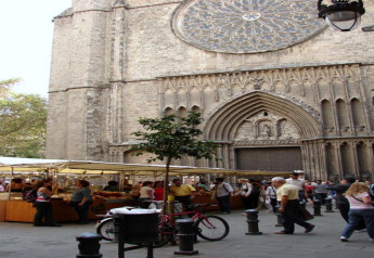 Straatmarkt in Spanje aan een grote gotische kerk, veel mensen, marktkraampjes en een gestalde fiets.