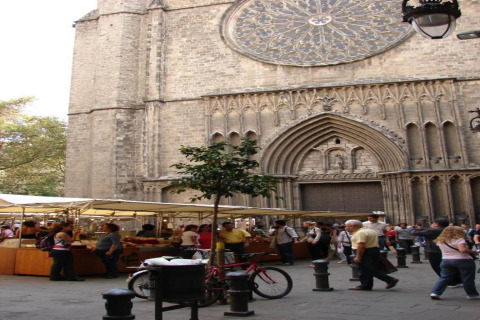 Mercado callejero en España frente a una gran iglesia gótica, gente, puestos y una bicicleta estacionada.