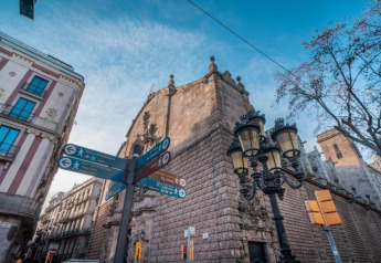 Señales peatonales y edificios antiguos en Barcelona, España, bajo cielo azul y farolas clásicas.