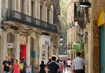 Mensen wandelen in een sfeervolle, smalle straat in Spanje met oude gebouwen en mooie balkons.
