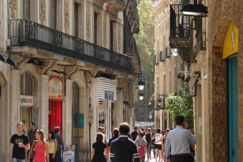 Personas paseando por una calle estrecha y encantadora en España, rodeada de edificios antiguos y balcones.