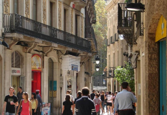 Personas paseando por una calle estrecha y encantadora en España, rodeada de edificios antiguos y balcones.