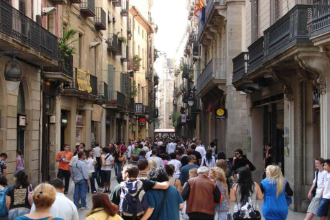 Calle abarrotada en España, personas recorren entre antiguos edificios con balcones, ambiente animado urbano.