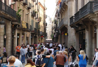 Calle abarrotada en España, personas recorren entre antiguos edificios con balcones, ambiente animado urbano.