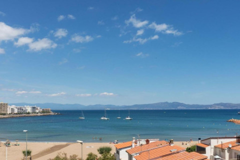 View from a glamping site overlooking the beach, blue sea with anchored boats, and orange-roofed cabins.