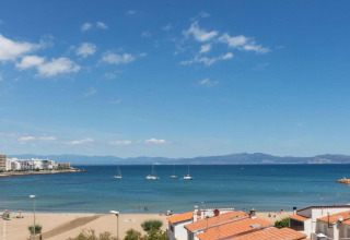 View from a glamping site overlooking the beach, blue sea with anchored boats, and orange-roofed cabins.