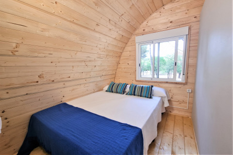 Cozy Nomad Paraiso pod bedroom in Spain, wood interior, double bed, window view of forest outside.