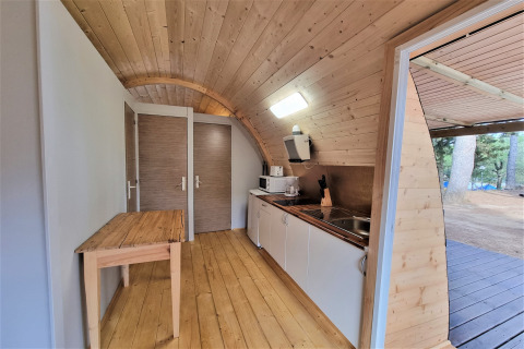 Interior of Nomad Paraiso pod in Spain featuring wood walls, compact kitchen and door open to nature.