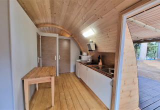 Interior of Nomad Paraiso pod in Spain featuring wood walls, compact kitchen and door open to nature.