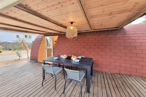 Outdoor dining area at Nomad Paraiso pod with wooden roof, table set for four and cozy atmosphere.