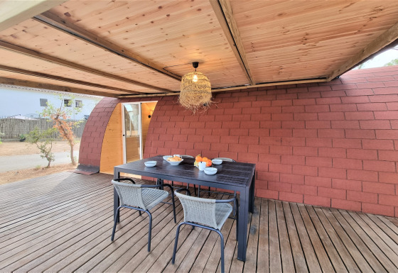 Outdoor dining area at Nomad Paraiso pod with wooden roof, table set for four and cozy atmosphere.