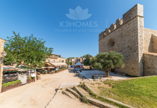 Photo of a glamping site with historic stone buildings, green space, trees, and outdoor dining area.