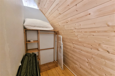Narrow room inside Nomad Paraiso pod in Spain with wood walls, shelf, folded chairs, and white pillow.