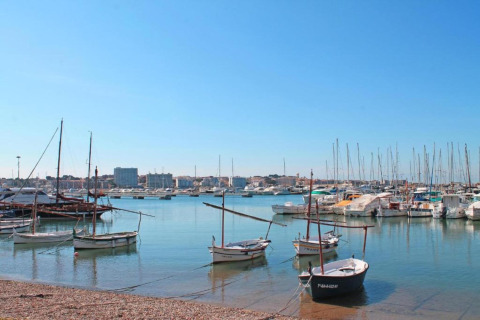 Boats anchored in the calm harbor at Nomad Paraiso in Spain, with clear skies and a coastal city backdrop.