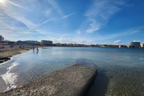 Photo of a beach at a glamping accommodation with people, calm water, and buildings in the distance.
