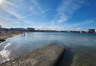 Photo of a beach at a glamping accommodation with people, calm water, and buildings in the distance.