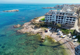 Aerial view of Nomad Paraiso in Spain, featuring seaside buildings, clear blue water, and small boats.