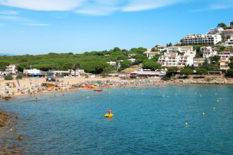 Photo of Nomad Paraiso beach in Spain with tourists, colorful umbrellas, and white buildings on a hill.