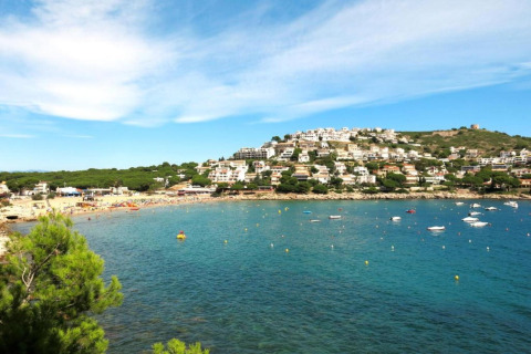 View from Nomad Paraiso pod in Spain, showing blue waters, boats, a sandy beach, and hillside houses.