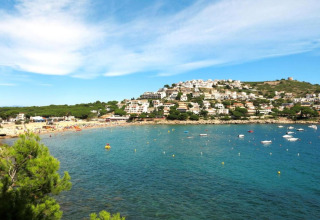 View from Nomad Paraiso pod in Spain, showing blue waters, boats, a sandy beach, and hillside houses.