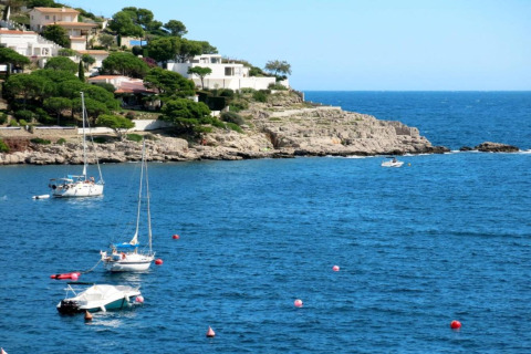Nomad Paraiso coast in Spain with boats moored in blue water, white villas, and lush green trees.
