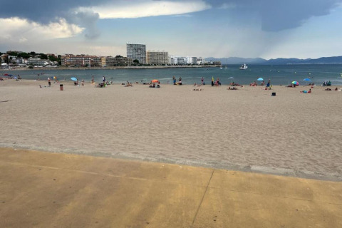 Beach view from Nomad Paraiso in Spain with sand, scattered umbrellas, the sea, and buildings in the background.