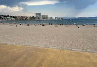 Beach view from Nomad Paraiso in Spain with sand, scattered umbrellas, the sea, and buildings in the background.